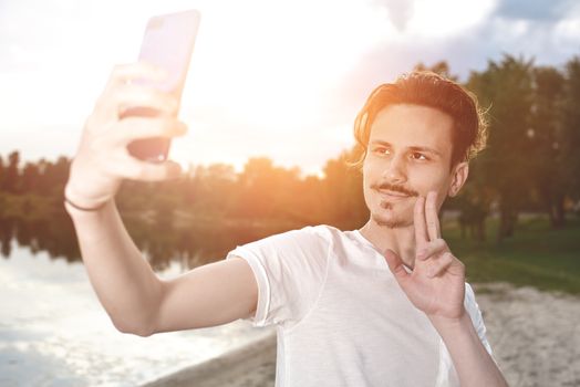 portrait of Young handsome stylish smiling guy makes selfie against the lake. beautiful nature