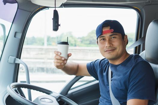 Close-up An Asian truck driver is driving and smiling happily. He has a white coffee cup in his hand.