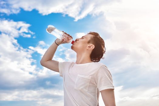 young guy drinks fresh water against of the lake and the forest background. summer thirst. beautiful view