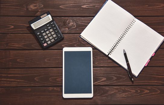 Top view of tablet, smartphone, calculator, notepad on wooden background, planning personal income, financial concept. typing on the calculator for money plan.