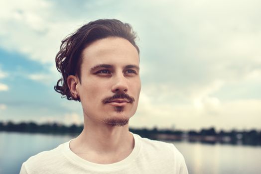 Portrait of Young Man Enjoys a beautiful view and looks into the distance near a lake and forest . summer . spring. nature