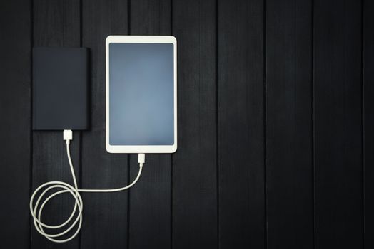 power bank loads tablet PC, smartphone - isolated on wooden background. charging concept. free copyspace