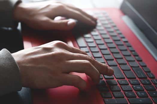 Side view shot of man's hands busy working on his laptop sitting at wooden table
