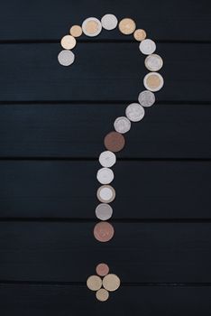 Scattered coins of different countries in the form of a question mark and an exclamation point on wooden table.