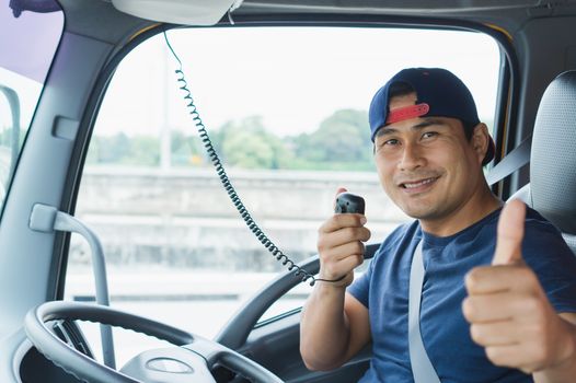 Close-up An Asian truck driver is driving and smiling happily. He is using radio to communicate.