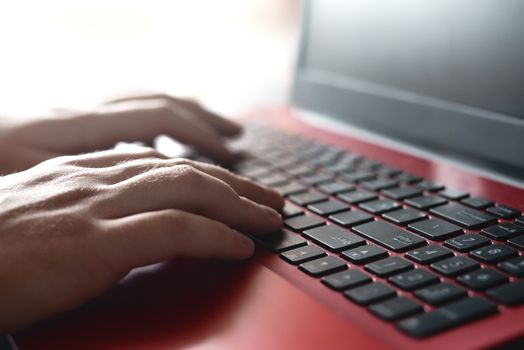 Side view shot of man's hands busy working on his laptop sitting at wooden table