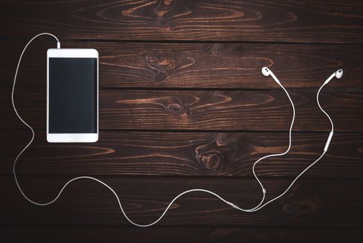 white smartphone with white headphones on wooden background- Image.Listening to music