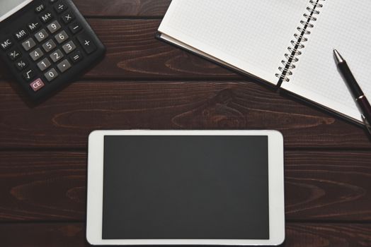 Top view of tablet, smartphone, calculator, notepad on wooden background, planning personal income, financial concept. typing on the calculator for money plan.