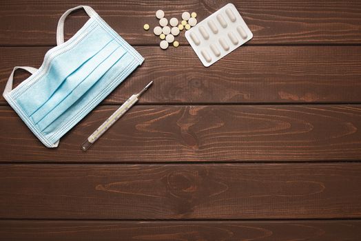 medical protective mask with medicines, thermometer on a wooden background, copy space