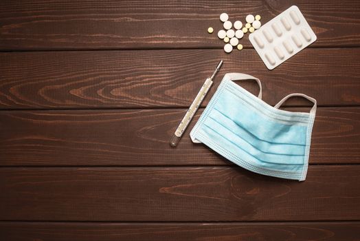 medical protective mask with medicines, thermometer on a wooden background, copy space