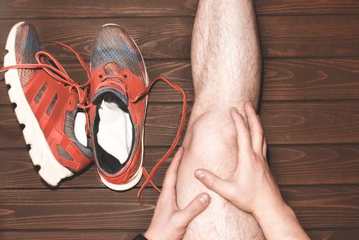 young sport man with strong athletic legs holding knee with his hands. in pain after suffering ligament injury during a running workout training on wooden background.