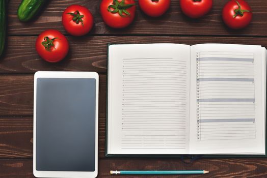 Dieting concept with a smartphone and a notepad and pen surrounded by lots of healthy fresh vegetables.