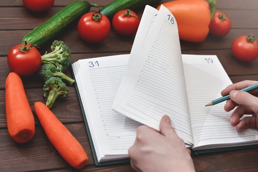 Dieting concept with a smartphone and a notepad and pen surrounded by lots of healthy vegetables.