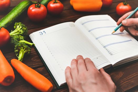 Dieting concept with a notepad and pen surrounded by lots of healthy fresh vegetables.