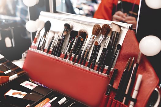 Closeup of makeup tools. Professional makeup brushes in tube, leather bag on a wooden table. Set of different objects for makeup artist in their holder.