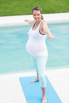 Pregnant woman doing yoga next to the swimming pool