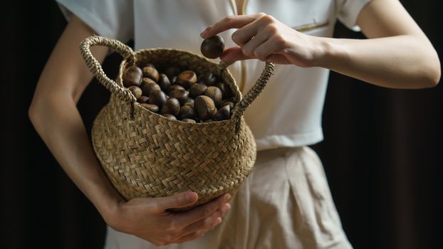 Person holding chestnuts on hand with wicker basket full of chestnuts.