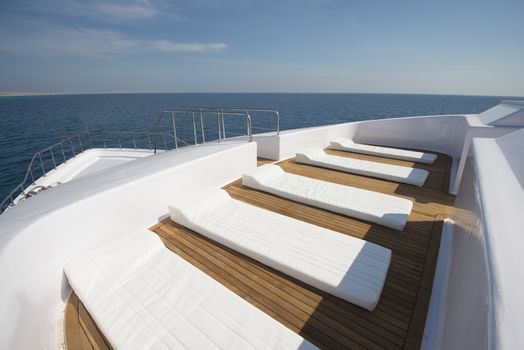 View over the bow of a large luxury motor yacht on tropical open ocean with sun beds