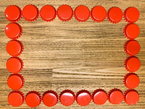 A frame made from red beer bottle tops lids on a rustic wooden table. Beer drinkers postcard concept, top view horizontal stock image with empty space for text