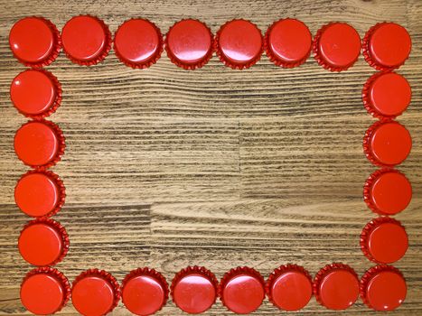 A frame made from red beer bottle tops lids on a rustic wooden table. Beer drinkers postcard concept, top view horizontal stock image with empty space for text