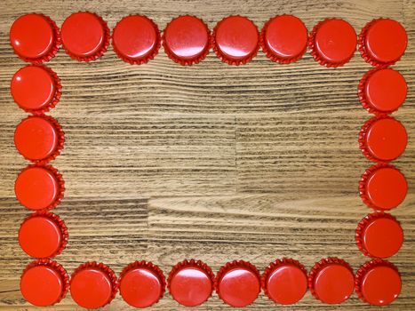 A frame made from red beer bottle tops lids on a rustic wooden table. Beer drinkers postcard concept, top view horizontal stock image with empty space for text