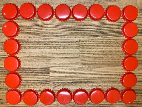 A frame made from red beer bottle tops lids on a rustic wooden table. Beer drinkers postcard concept, top view horizontal stock image with empty space for text