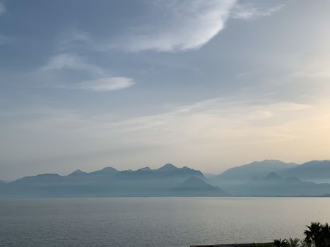 Cloudy blue sky over Mediterranean sea with mountains silhouettes. Horizontal stock image.