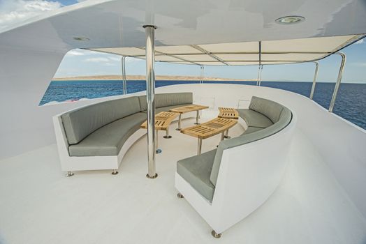 Sundeck area of a large luxury motor yacht with chairs sofa table and tropical sea view background