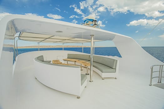 Sundeck area of a large luxury motor yacht with chairs sofa table and tropical sea view background