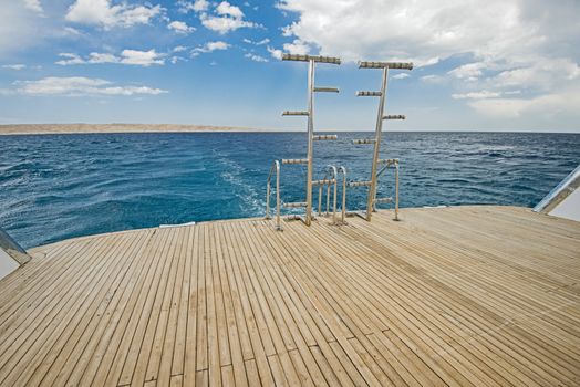 Metal steel ladders on back teak deck of a luxury motor yacht sailing on a tropical ocean with cloudy sky background