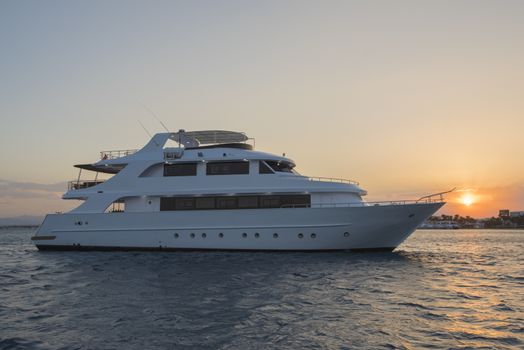 Large private luxury motor yacht boat sailing out on a tropical sea ocean lit up at dusk with sunset background