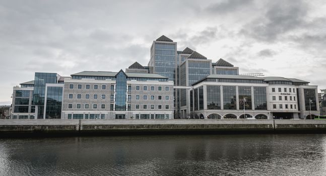 Dublin, Ireland - February 12, 2019: View of the modern building of the Irish commercial bank Ulster Bank next to the River Liffey where people walk on a winter day