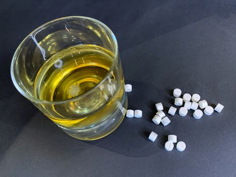 A glass of whiskey with ice and a lot of white pills on a gray background. Suicide concept with tablets and alcohol. Stock image.