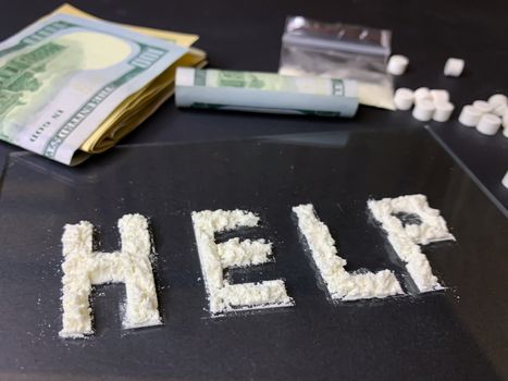 Pills, us dollar banknotes and cocaine  on a gray background. Stop drugs concept. A word "help" written with cocaine. Stock image.