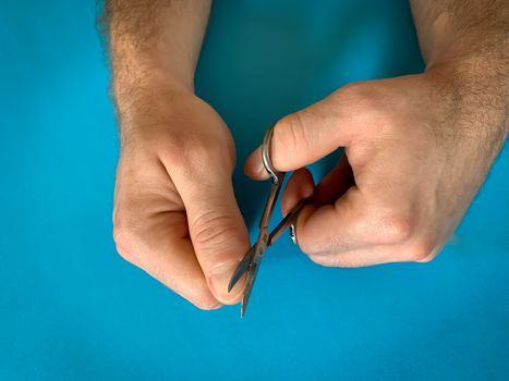 Male's hand holding on nail scissors, Man use nail scissors cutting their thumbs nail on blue background
