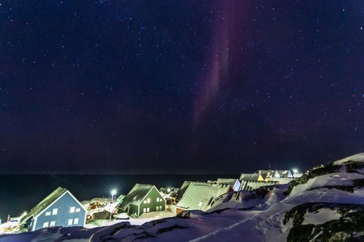 Arctic polar night over colorful inuit houses with small northern light in a suburb of arctic capital Nuuk, Greenland