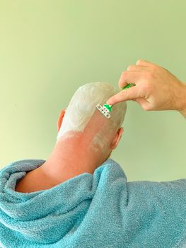 Young man shaving his head by himself, view from back