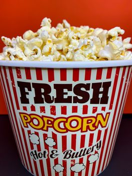 Close up delicious fresh buttery popcorn in a stripped red and white bowl on red background