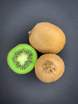 Fresh ripe whole and half kiwi fruit on a gray background. Vertical flat lay