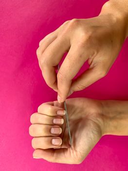 Woman's girl's hand filing nails with metal nail file on a pink background. Self manicure at home