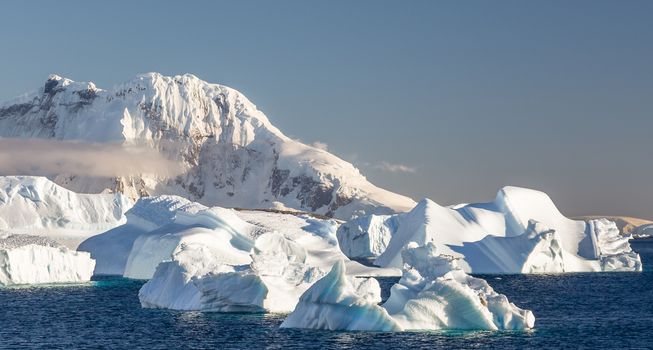 Icebergs on the still waters of Cuverville island with snowy mountains and glacier in the background, Antarctica