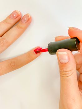 Close up female woman painting her nails with nail polish in red color on a white background. Self manicure at home