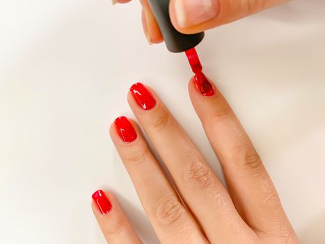 Close up female woman painting her nails with nail polish in red color on a white background. Self manicure at home