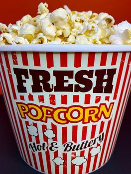 Close up delicious fresh buttery popcorn in a stripped red and white bowl on red background