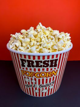 Close up delicious fresh buttery popcorn in a stripped red and white bowl on red background