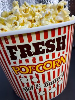 Close up delicious fresh buttery popcorn in a stripped red and white bowl on gray background