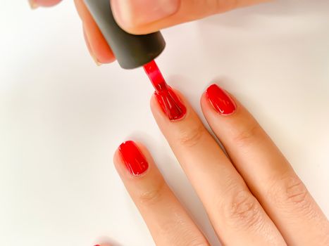 Close up female woman painting her nails with nail polish in red color on a white background. Self manicure at home