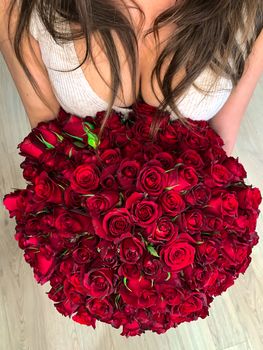 A young girl holding in hands a huge bouquet of 101 wonderful red roses. Top view