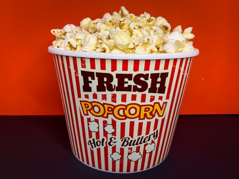 Close up delicious fresh buttery popcorn in a stripped red and white bowl on red background