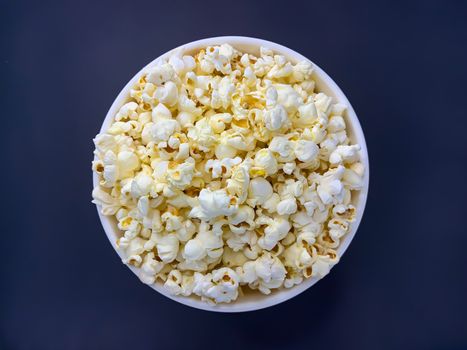 Close up delicious fresh buttery popcorn in a bowl on dark blue background. Flat lay view